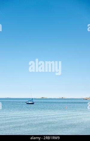 Ruhige Meereslandschaft mit einem Segelboot auf ruhigem türkisfarbenem Wasser mit großem, klaren blauen Hintergrund ohne Wolken für ein nautisches, ruhiges Konzept Stockfoto