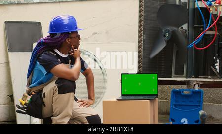 afroamerikanischer Spezialist bestellt neue interne Teile auf Chroma Key Laptop wegen Fehlfunktion des Kondensators nach Abschluss der Wartung. Kompetenter Elektriker, der online nach Ersatzteilen für Kondensatoren sucht Stockfoto