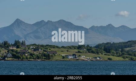 Isle of Skye, Schottland, Vereinigtes Königreich. 6. Juni 2023 Panoramablick auf die Cuillin-Berge über grüne Landschaft und Wohnhäuser auf der Isle of Skye. Stockfoto