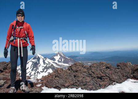 Erwachsene Frau steht auf dem Gipfel der South Sister mit den Cascade Mountains dahinter. Oregon Stockfoto