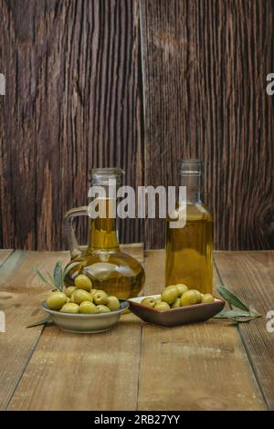 Stillleben mit zwei Glasbehältern gefüllt mit nativem Olivenöl zusammen mit einigen Tellern mit Oliven Stockfoto