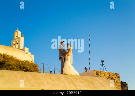 Frisch verheiratete Paare, die auf dem Dach des Höhlenhauses auf den Klippen in Fira, der Hauptstadt Santorins, eine Fotosession machen – ein beliebtes Hochzeitsziel Stockfoto