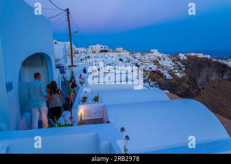 Touristen laufen durch die engen Gassen und weißen Häuser des Luxus-Resort-Dorfes Imerovigli auf den Klippen mit Blick auf die Caldera in der Dämmerung, Griechenland Stockfoto