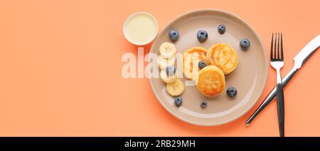 Teller mit leckeren Hüttenkäse-Pfannkuchen, Heidelbeere, Banane und Kondensmilch auf orangefarbenem Hintergrund mit Platz für Text Stockfoto