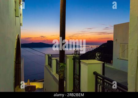 Enge Straße, die zur Caldera führt, mit wunderschönem Sonnenuntergangshimmel in Fira auf zerklüfteten steilen vulkanischen Klippen, Therasien-Insel in der Ferne, Santorin Stockfoto