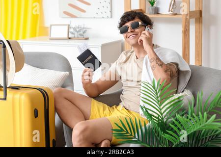 Ein junger Mann, bereit für den Sommerurlaub, der zu Hause per Handy telefoniert Stockfoto