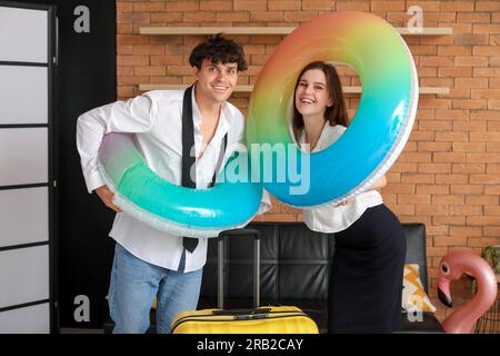 Ein junges Paar mit Schwimmringen und einem Koffer, bereit für den Sommerurlaub im Büro Stockfoto