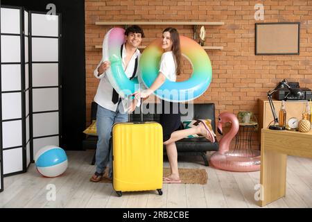 Ein junges Paar mit Schwimmringen und einem Koffer, bereit für den Sommerurlaub im Büro Stockfoto