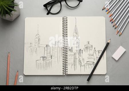 Skizze der Stadtlandschaft in Notizbuch, Bleistiften, Radiergummi und Brille auf grauem Tisch, flach liegend Stockfoto