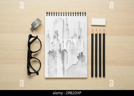 Skizze der Stadtlandschaft in Notizbuch, Bleistiften, Radiergummi und Gläsern auf Holztisch, flach liegend Stockfoto