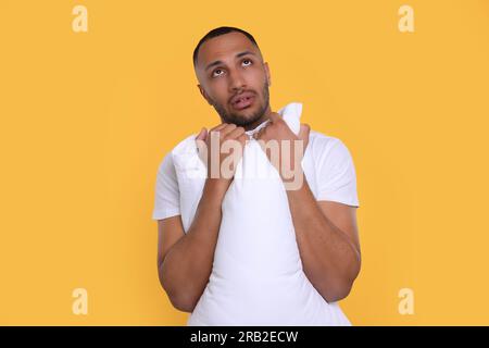 Müder Mann mit Kissen auf orangefarbenem Hintergrund. Schlaflosigkeit-Problem Stockfoto