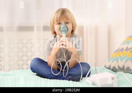 Kranker kleiner Junge mit Vernebler zur Inhalation am Bett zu Hause Stockfoto