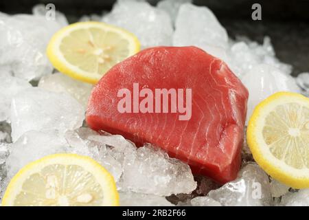 Frisches rohes Thunfischsteak mit Zitrone und Eis auf schwarzem, rustikalem Hintergrund Stockfoto