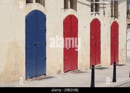 Eine Reihe von vier Türen in Primärfarben auf einem Block abschließbarer Lagereinheiten am Straßenrand in Valletta, Hauptstadt von Malta, April 2023. Stockfoto
