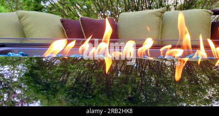 Glaskamin neben Terrassenmöbeln und mit einer Baumreflektierung auf dem Glas Stockfoto