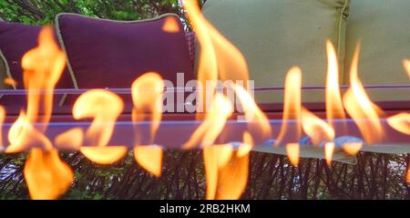 Glaskamin neben Terrassenmöbeln und mit einer Baumreflektierung auf dem Glas Stockfoto