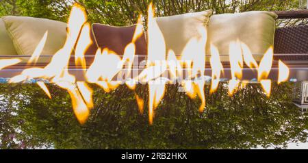 Glaskamin neben Terrassenmöbeln und mit einer Baumreflektierung auf dem Glas Stockfoto