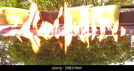 Glaskamin neben Terrassenmöbeln und mit einer Baumreflektierung auf dem Glas Stockfoto