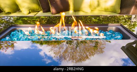 Glaskamin neben Terrassenmöbeln und mit einer Baumreflektierung auf dem Glas Stockfoto