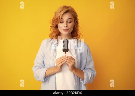 Junge Frau isst köstliches Eis, isst gefrorenes Dessert, trägt lässige Kleidung, isoliert auf gelbem Hintergrund Stockfoto