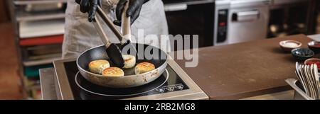 Professioneller Koch bereitet Käsekuchen auf Bratpfanne zum Frühstück in der Restaurantküche zu Stockfoto