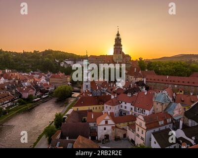 Luftaufnahme von Cesky Krumlov entlang der Moldau mit St. Jost-Kirche, mittelalterlicher Burg und Häusern mit rotem Dach, atemberaubender kalter dramatischer Sonnenuntergang Stockfoto