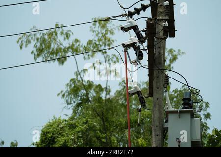 Elektriker, der einen Klemmstab verwendet, um einen abgefallenen Sicherungsausschnitt am vom Isolator unterstützten Hochspannungs-Strommast zu reparieren. Stockfoto