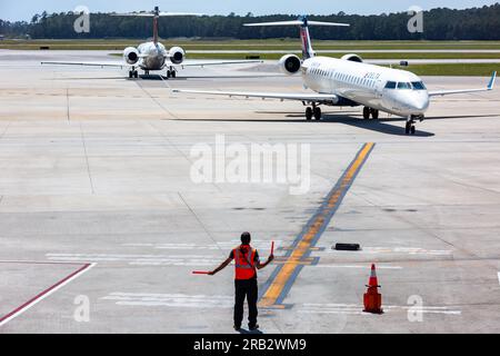 Ein Marshaller leitet einen Passagierjet von Delta Airlines auf einen Parkplatz, während ein anderes Taxi auf dem Rollweg am Myrtle Beach International Airport, SC, fährt. Stockfoto