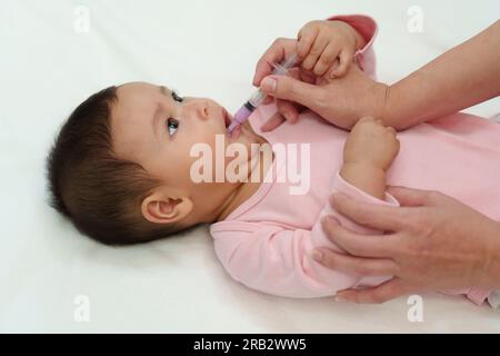 Mutter füttert krankes Säugling mit einer Spritze mit einem flüssigen Medikament Stockfoto