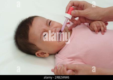 Krankes Säuglingsbaby weint, während es sich weigert, flüssige Medizin mit einem Tropfer zu essen Stockfoto