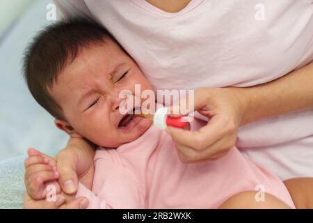 Krankes Säuglingsbaby weint, während es sich weigert, flüssige Medizin mit einem Tropfer zu essen Stockfoto