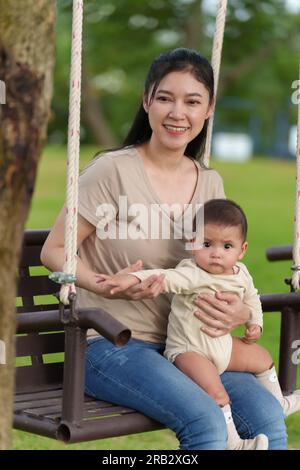 Mutter mit ihrem Baby sitzt auf einer Schaukel im Park Stockfoto