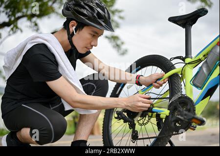 Ein professioneller junger asiatischer Radfahrer repariert seine Fahrradkette auf der Straße, nachdem er auf Landstraßen gefahren ist. Wartung, Reparatur Stockfoto