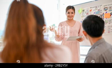 Eine zuversichtliche und attraktive asiatische Technikentwicklerin präsentiert ihren Kollegen ihr Projekt und erstellt im Meeting ein Brainstorming zu einem neuen Projekt Stockfoto