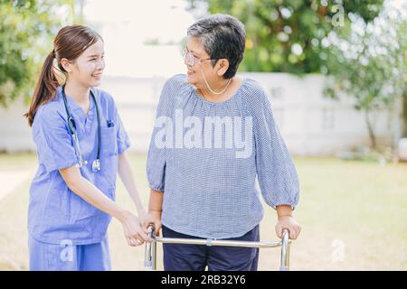 Junge Krankenschwester hilft asiatischer Seniorin beim Gehen. pflegekraft, die alte Patientin im Pflegeheim unterstützt. Der Altengang mit Gehhilfe in der häuslichen Pflege. Stockfoto