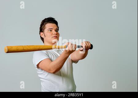 Ein Mann mit einem Schläger in der Hand schwingt auf grauem Hintergrund Stockfoto