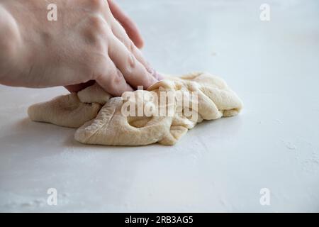 Weibliche Hände kneten rohen Teig auf einen weißen Tisch in der Küche, Teig Stockfoto