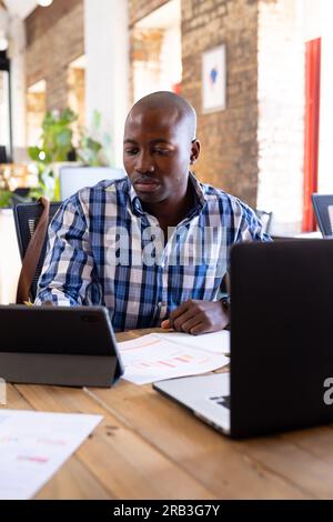 Fokussierter afroamerikanischer Gelegenheitsunternehmer, der Tablet in einem kreativen Büro verwendet. Geschäft, Arbeit und Technologie unverändert. Stockfoto