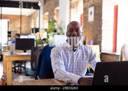 Porträt eines glücklichen afroamerikanischen Gelegenheitsgeschäfts, der ein Notebook im Kreativbüro benutzt. Geschäft, Technologie und Arbeit, unverändert. Stockfoto