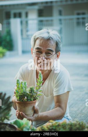 Glücksgesicht eines asiatischen Seniorenmannes mit saftiger Hauspflanze in der Hand Stockfoto