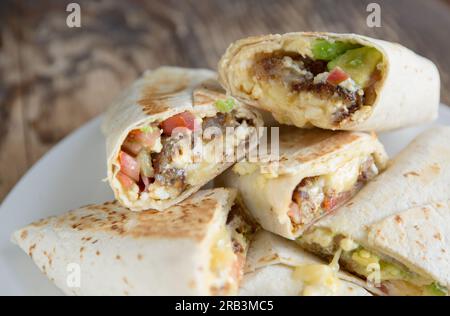 Ein hausgemachter Frühstücks-Burrito mit Avocado, Tomaten, gebratener Kartoffel, Speck, Käse und Rührei, verpackt in einer Tortilla. England GB Stockfoto