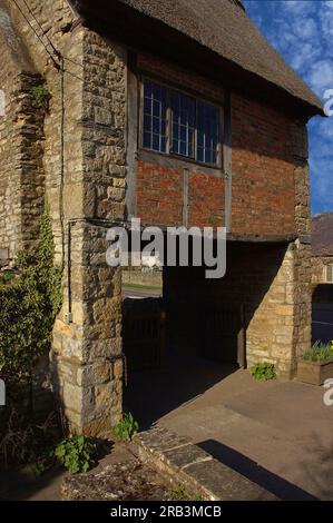 Hütte aus dem späten 16. Oder frühen 17. Jahrhundert, unterschnitten zu einem Lych-Tor, das zur mittelalterlichen Cotswold Parish Church of St Peter and St Paul in Long Compton, Warwickshire, England führt. Stockfoto