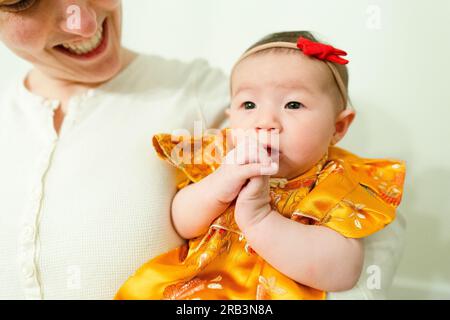 Das niedliche Mädchen schnallt sich die Hände, während die Mutter sie anlächelt Stockfoto