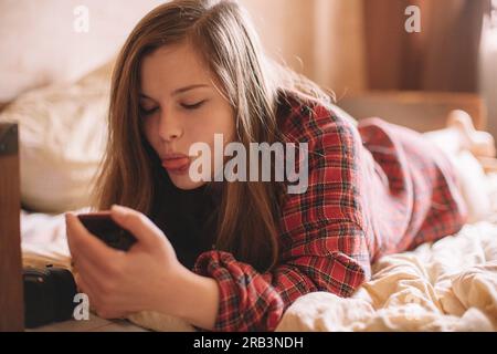 Teenager-Mädchen, die ihre Zunge festhält, während sie ihr Smartphone auf dem Bett liegend benutzten Stockfoto