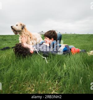 Vater und Sohn lagen mit ihrem Hund im hohen Gras an einem Frühlingstag Stockfoto