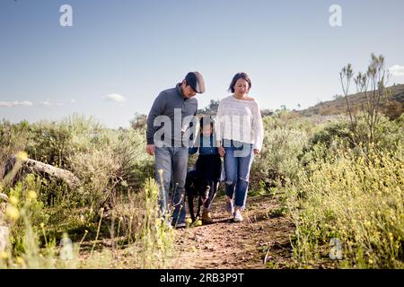 Eine dreiköpfige asiatische Familie, die mit dem Hund in San Diego durch das Feld spaziert Stockfoto