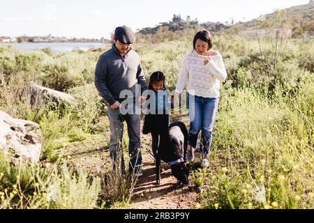 Eine dreiköpfige asiatische Familie, die mit dem Hund in San Diego durch das Feld spaziert Stockfoto