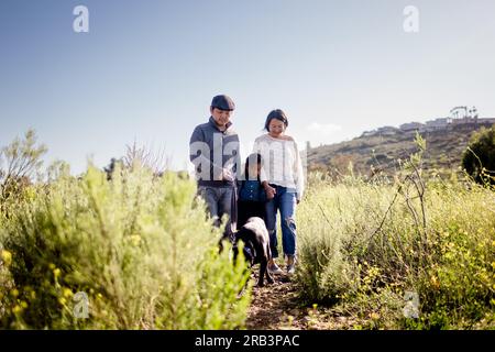 Eine dreiköpfige asiatische Familie, die mit dem Hund in San Diego durch das Feld spaziert Stockfoto