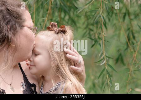 Ein kleiner Kuss von mom vor einer weinenden Weide Stockfoto