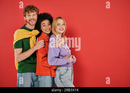 Polyamoröses Konzept, drei wechselrassische Liebhaber umarmen sich gegenseitig, kulturelle Vielfalt, Polygamie, glückliche, multiethnische Menschen, die vor die Kamera schauen, Stockfoto